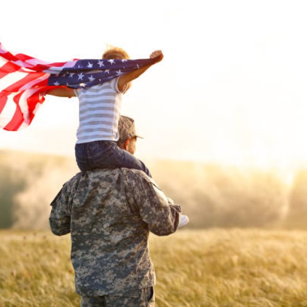 Rear view of military man father carrying happy little son with american flag on shoulders and enjoying amazing summer nature view on sunny day, happy male soldier dad reunited with son after US army